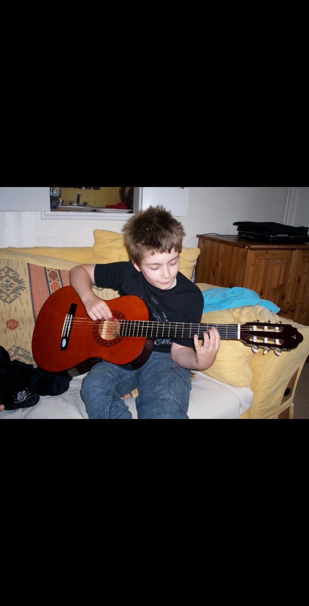 Young guitarist practising at home on the sofa