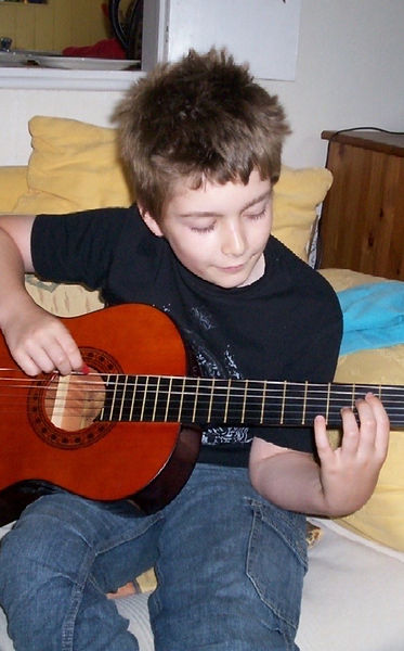 Callum Garland as a young boy, playing a nylon-string guitar